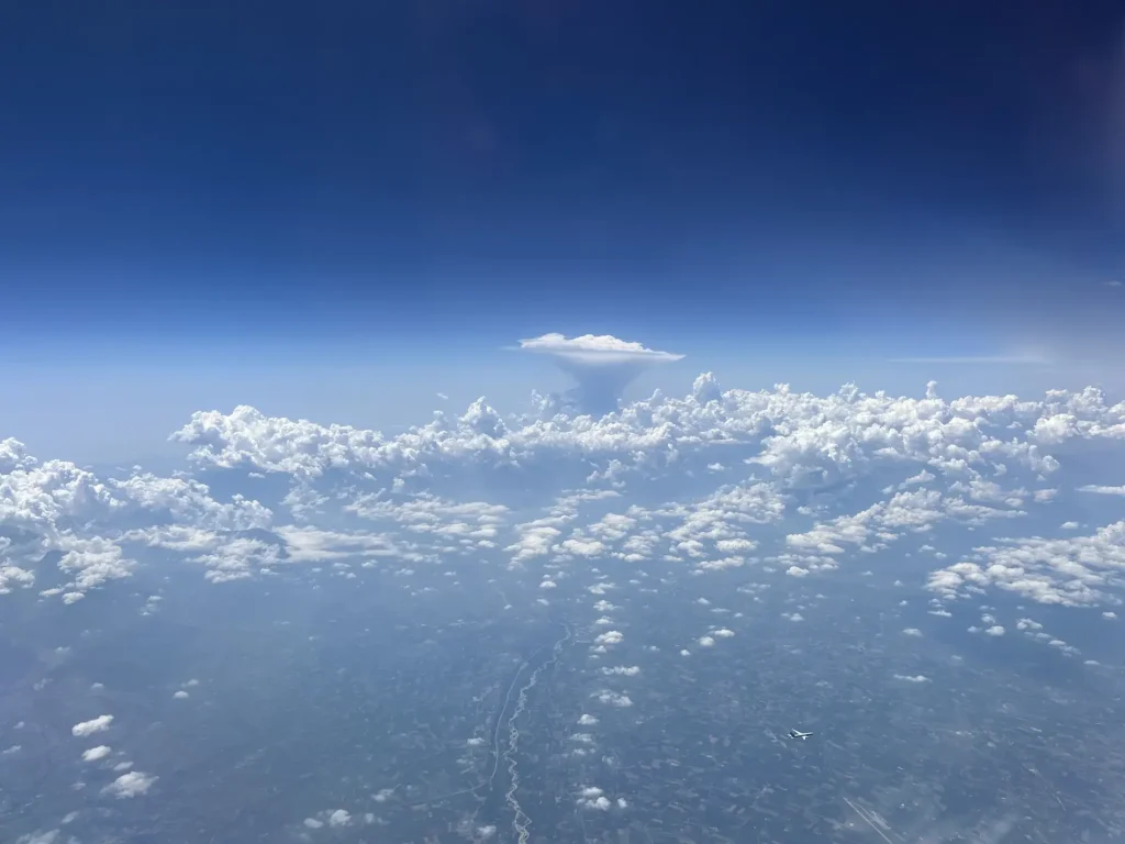 Vue aérienne d'un ciel bleu avec nuages cotonneux et un nuage en enclume surplombant un paysage brumeux.